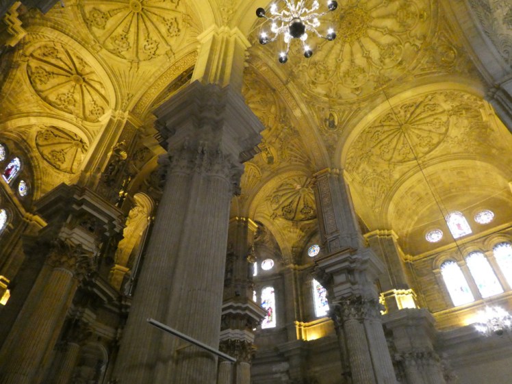 The heavy pillars holding up a very ornate ceiling. The ceiling is illuminated in sodium orange lights.
