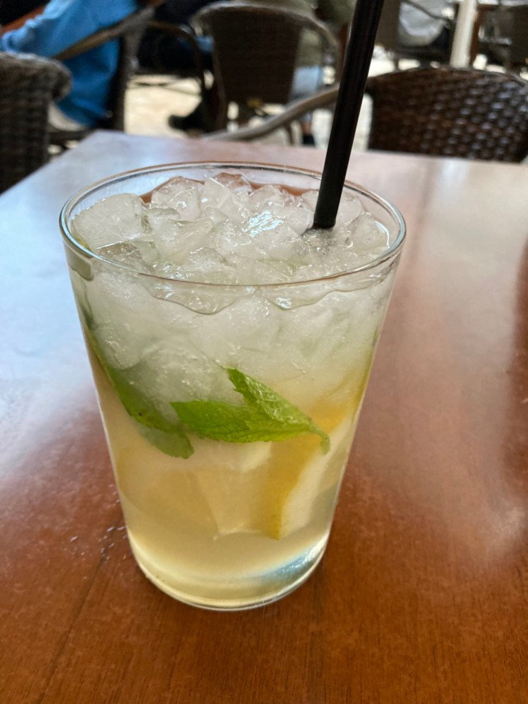 A glass of homemade lemonade with a straw in it. The top is full of ice and the bottom is slightly opaque with sugar syrup. There's a slice of lemon in there and a few mint leaves.