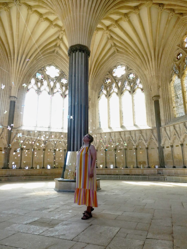 Me in a long striped dress of pinks, oranges and yellows in the Chapter House of Wells Cathedral while wearing my dark pink The North Face sandals.