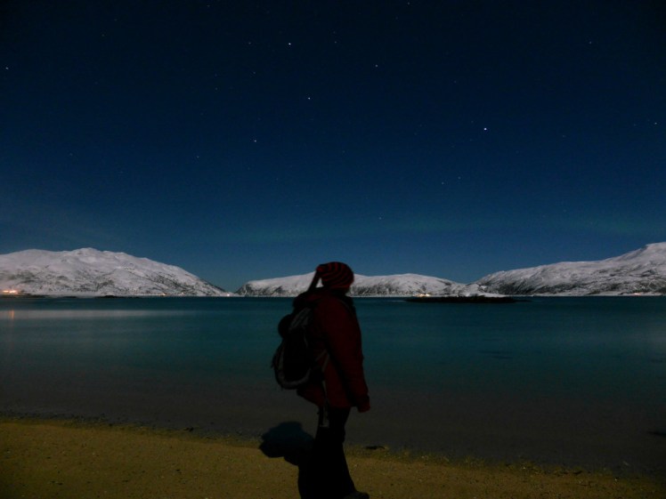 Me standing by the edge of a fjord in Norway at the dead of night. If you look closely, you can make out a faint line of Northern Lights over the lake.