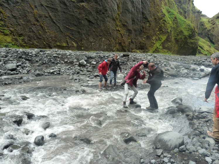 The rest of the tour group balancing precariously on rocks in quite a rushing grey river.