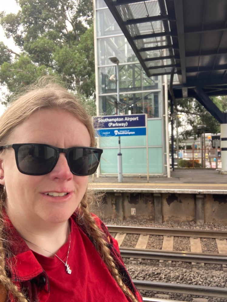 A selfie in a red t-shirt and red & black checked shirt on the platform at Southampton Airport Parkway station.