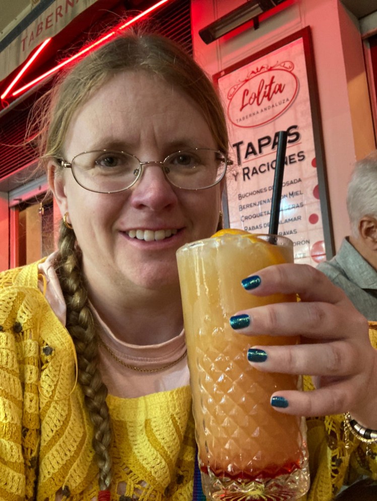 A selfie holding a large yellow fruity drink with a bit of red in the bottom and a straw.