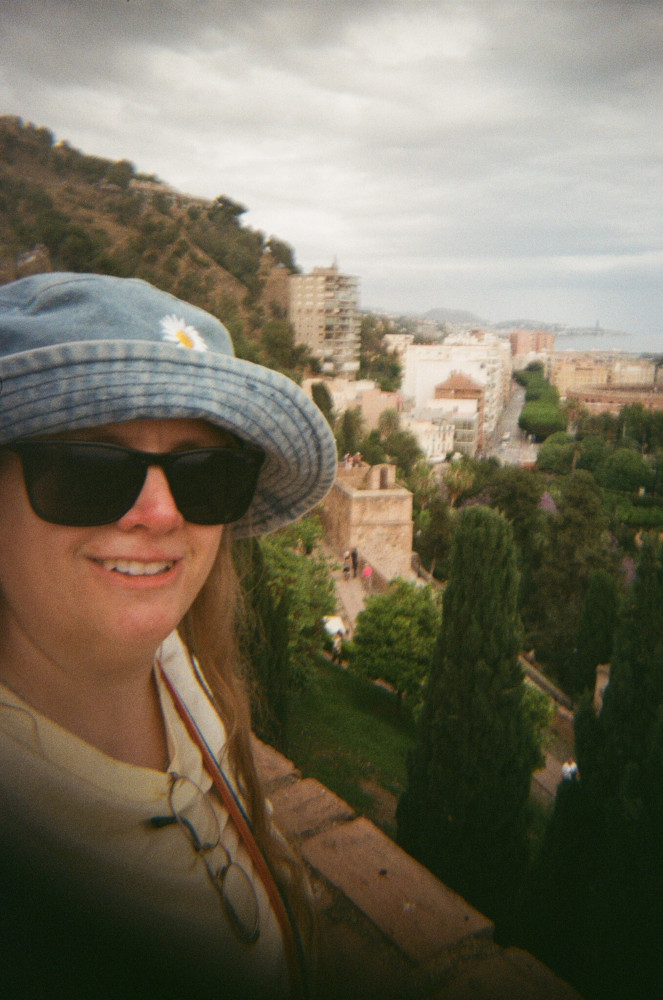 A selfie at the Alczaba in a yellow t-shirt and a denim bucket hat with a daisy on it.