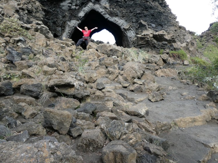 A timer selfie showing me, high up a stack of rocks in the entrance to a lava "bubble" with my arms outstretched.