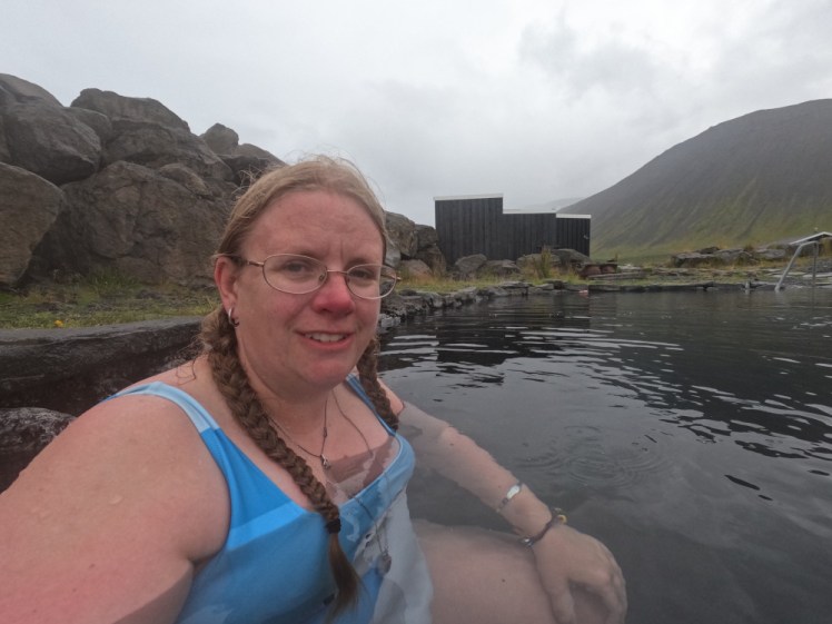 A selfie in Grettislaug, a pool with a stone surround, protected from the sea by a stone wall, on a very overcast evening.