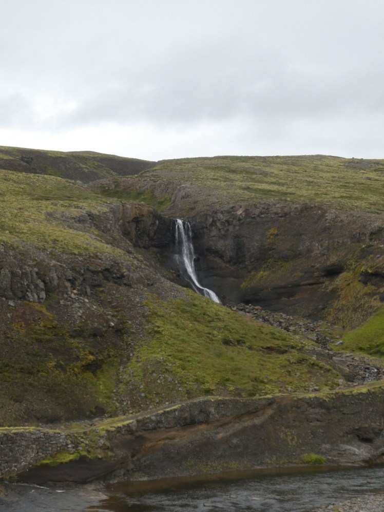A small waterfall that has carved out a chunk of the hillside, tumbling down into a stream that runs parallel to the Ring Road.