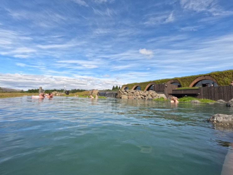 The upper lagoon at Laugarás. The back wall is formed by the same low, arched, turf-covered building as the front and the water is turquoise under a blue sky.