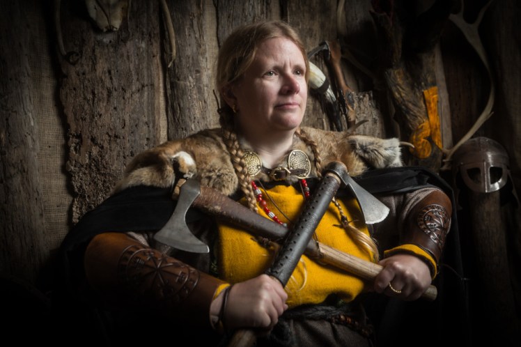 Me dressed as a Viking with lots of furs and layers and plaits and no glasses, holding two hatchets up crossed in front of me.