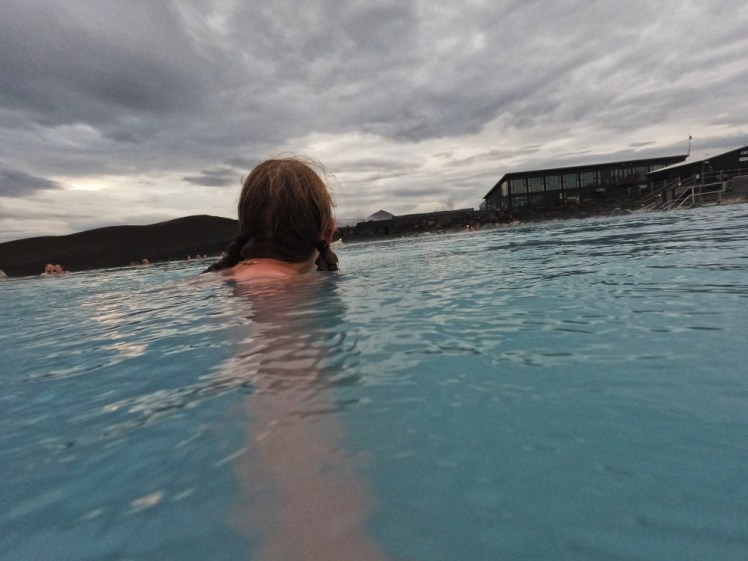 The back of my head in Myvatn Nature Baths as the sun gets low. The water is still quite bright blue but the sky is cloudy and the sunset has reached the white stage.