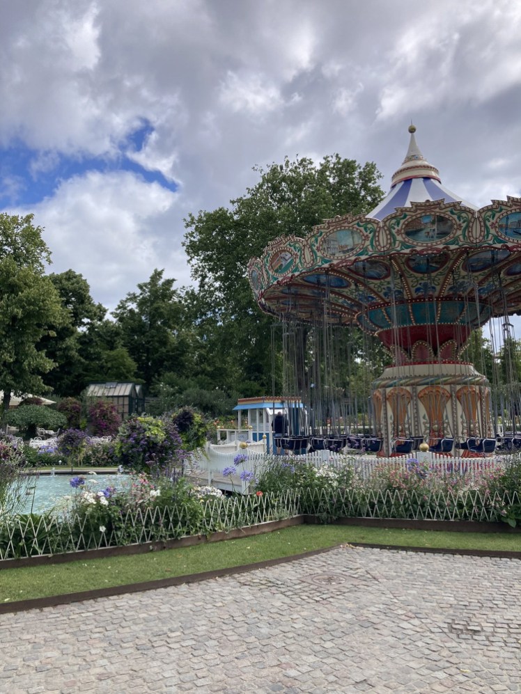 An old-fashioned carousel with swings instead of animals to ride, in the middle of the gardens. There are decorative low hedges, there's a large water feature next to it and there are even some mini greenhouses in the background, although I think they're repurposed as bars or snack kiosks by now.