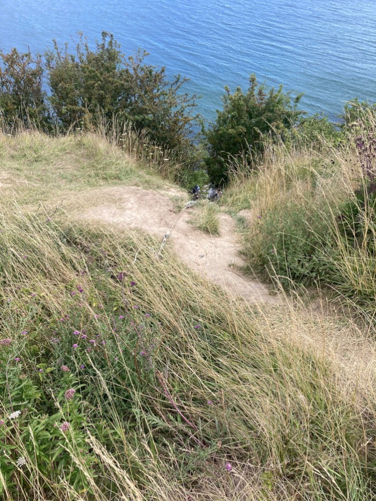 The dusty footpath that leads abruptly over the edge of the cliff. If you look closely, there's a tatty rope and the top of heads just visible below the grass.