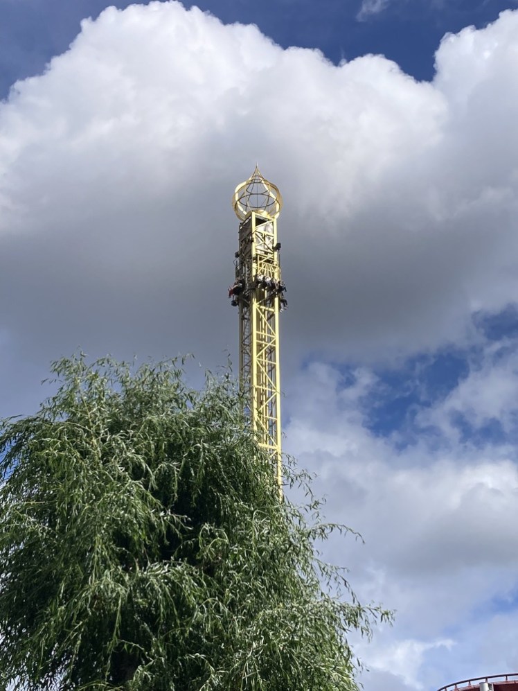 The Golden Tower, a gold needle sticking out from the trees with riders mid free-fall near the top.
