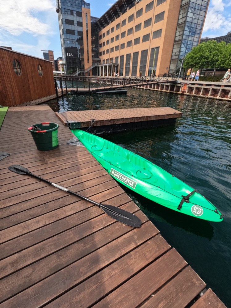 The kayak tied up again at Green Island, with the slim-bladed paddle and the bucket of rubbish on the decking next to it.