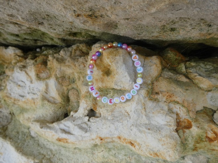 An Eras-style bead bracelet with multicolour letters spelling out "In my cenozoic era" hanging from a bit of rock among the fish clay.