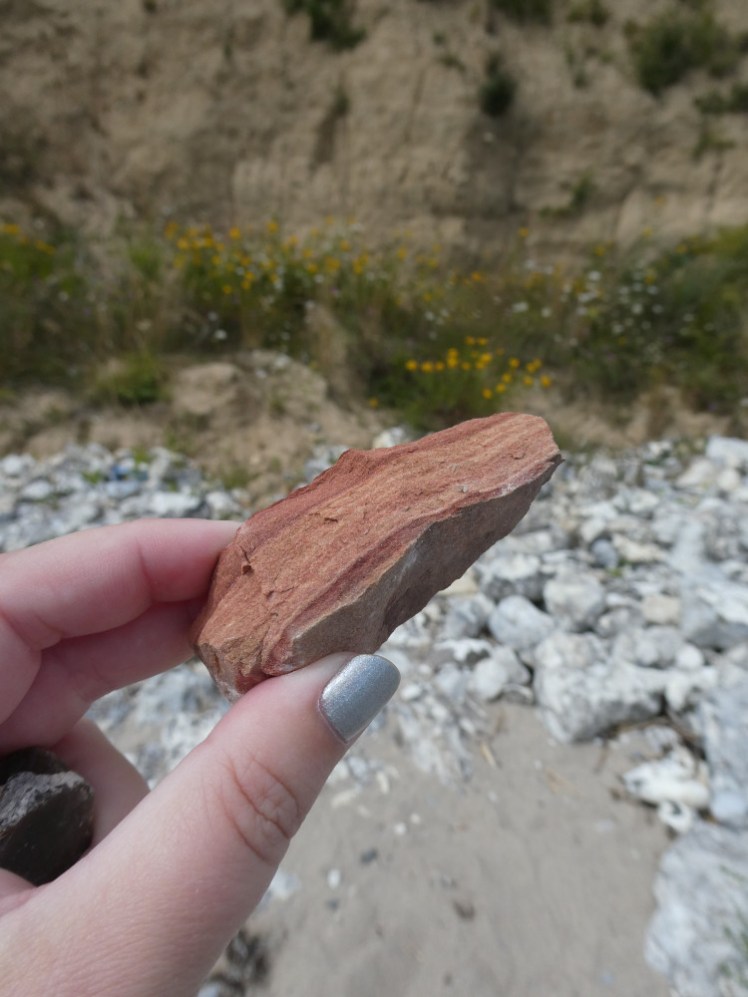 A piece of red striped rock, which really doesn't fit in with the white and grey rock on the beach and in the cliff.
